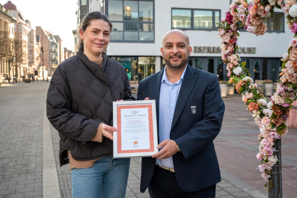två personer visar upp diplom bredvid blomsterhjärta