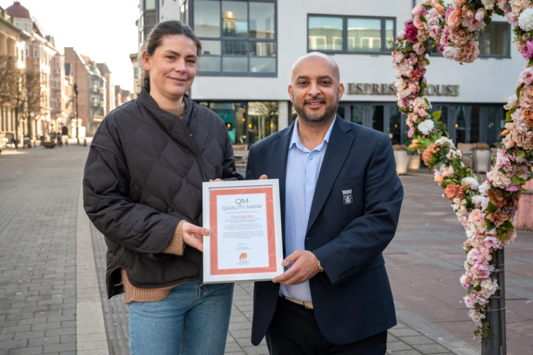 två personer visar upp diplom bredvid blomsterhjärta